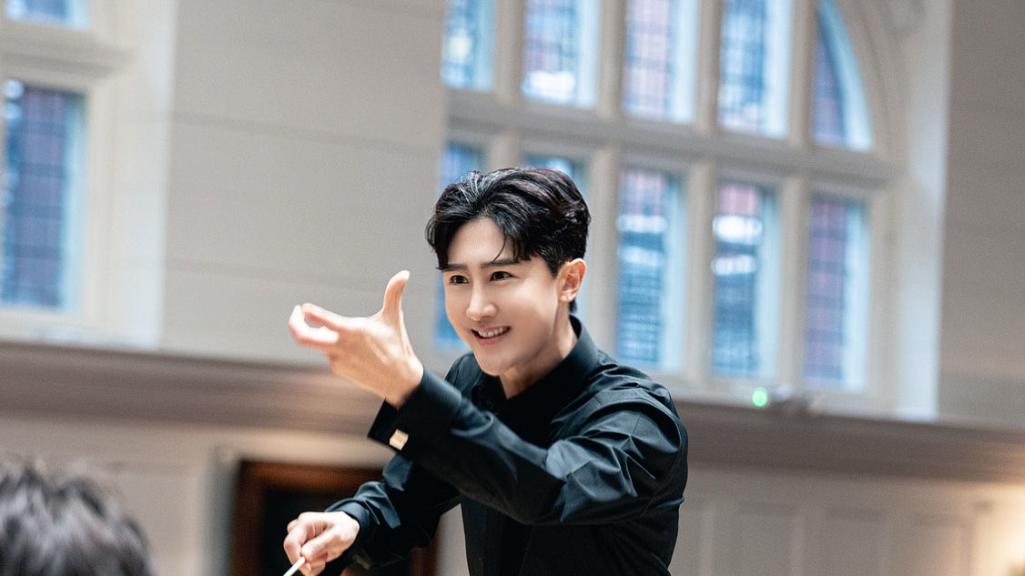 An Asian male student conducting an orchestra rehearsal.